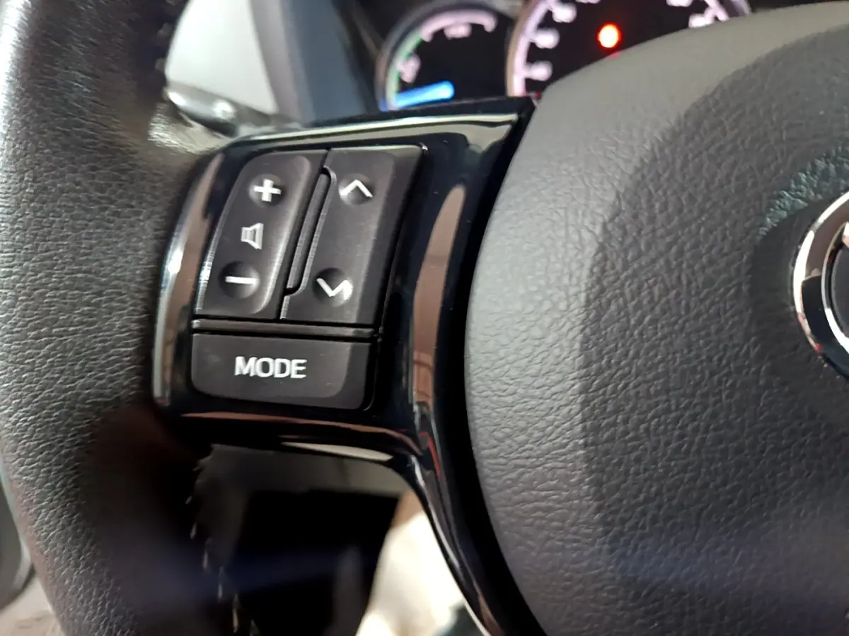 Gros plan sur le volant cuir et alu de la Toyota Yaris blanche, avec commandes multifonctions côté gauche.