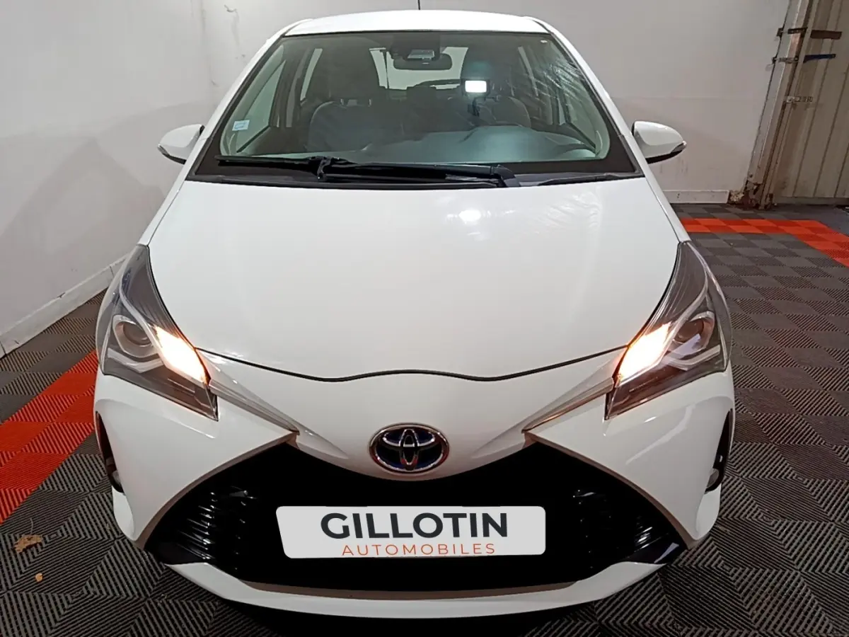 Vue avant d'une Toyota Yaris blanche 2019 avec phares allumés et calandre noire distinctive.