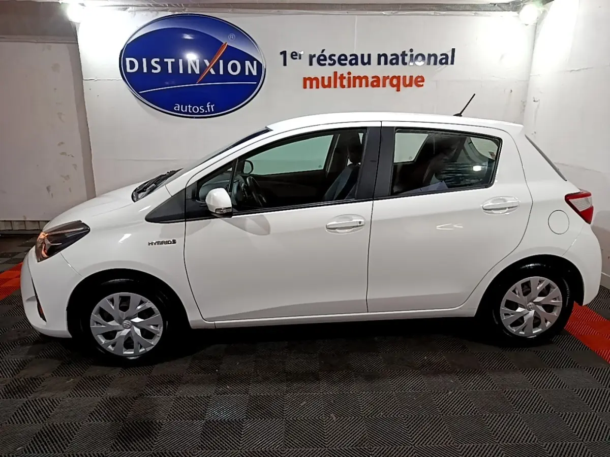 Vue de profil côté gauche d'une Toyota Yaris blanche hybride 2019, avec logo Hybrid visible sur l'aile avant.