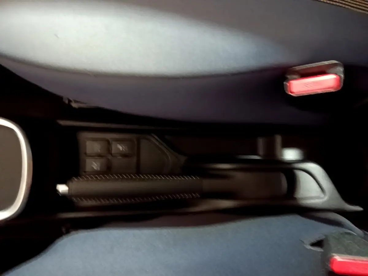 Vue rapprochée de la console centrale de la Toyota Yaris blanche, montrant le frein à main et les boutons de commande.