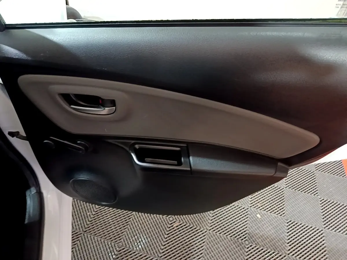 Vue intérieure du panneau de porte avant gauche de la Toyota Yaris blanche, avec poignée et haut-parleur intégrés.