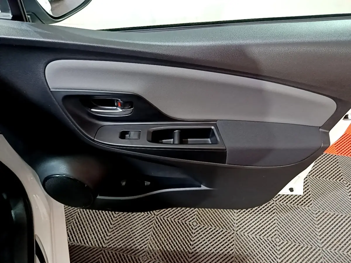 Vue rapprochée de la porte avant gauche de la Toyota Yaris blanche, montrant la poignée intérieure et les commandes de fenêtre.
