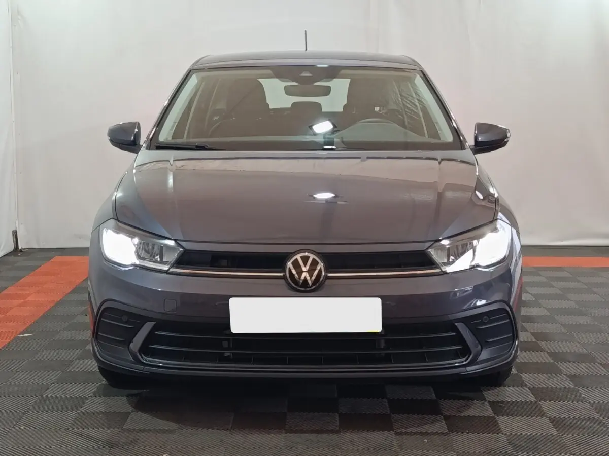 Vue frontale d'une Volkswagen Polo gris foncé 2025 avec phares LED allumés dans un studio.