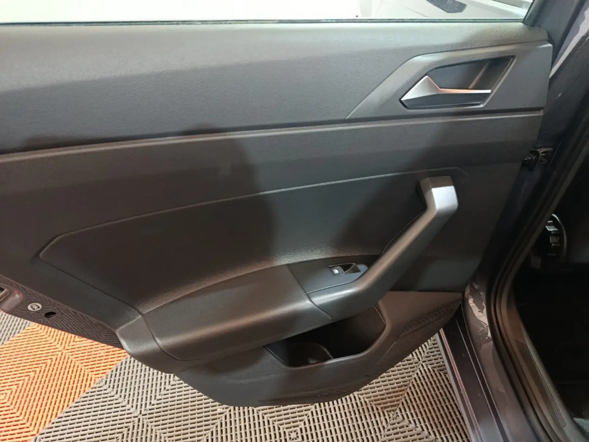 Vue rapprochée de la porte intérieure côté gauche gris foncé de la Volkswagen Polo 2025 avec poignée angulaire et bouton de vitre électrique.