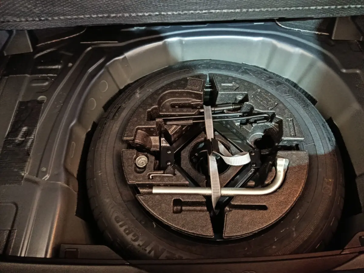 Vue en plongée du coffre d'une Volkswagen Polo gris foncé, montrant la roue de secours et les outils de bord.