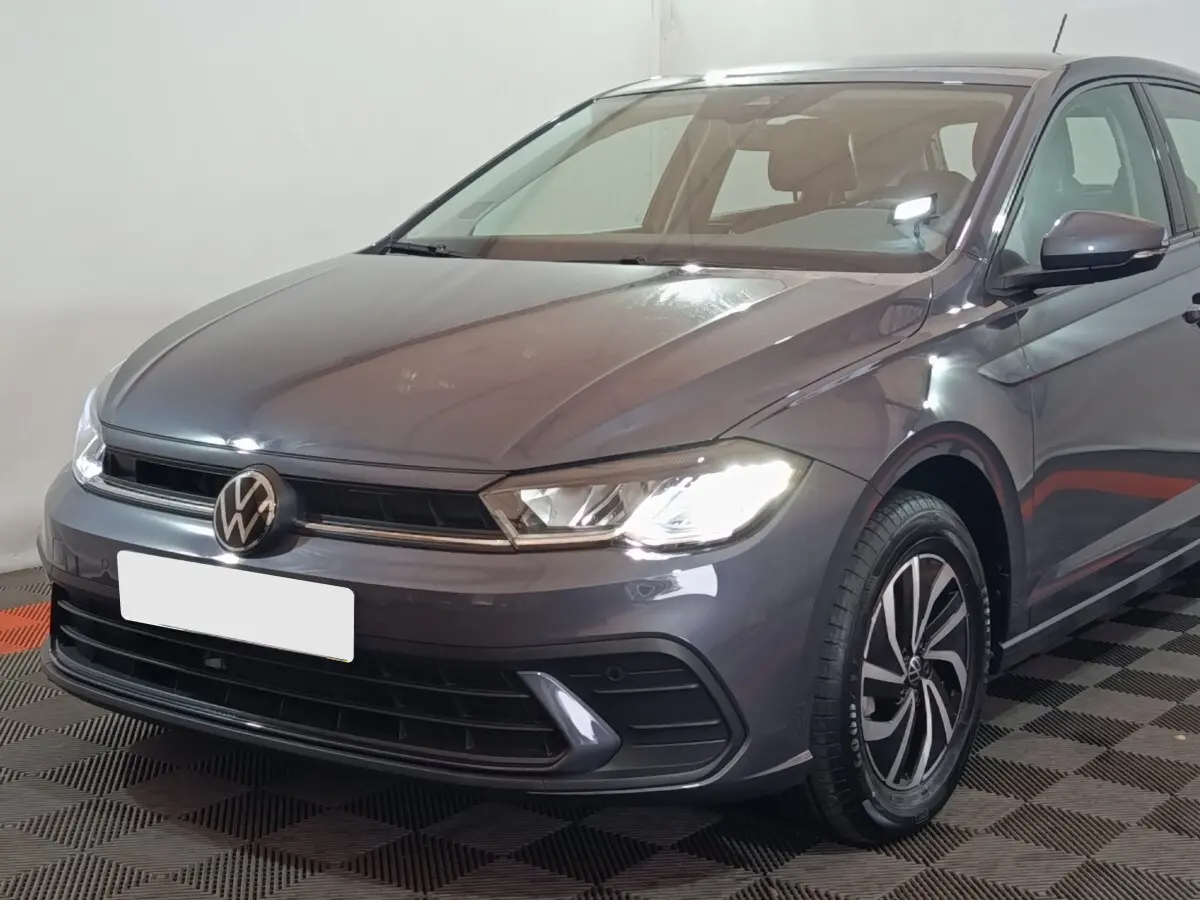 Volkswagen Polo gris foncé vue 3/4 avant droit avec phares allumés et jantes alliage distinctives.