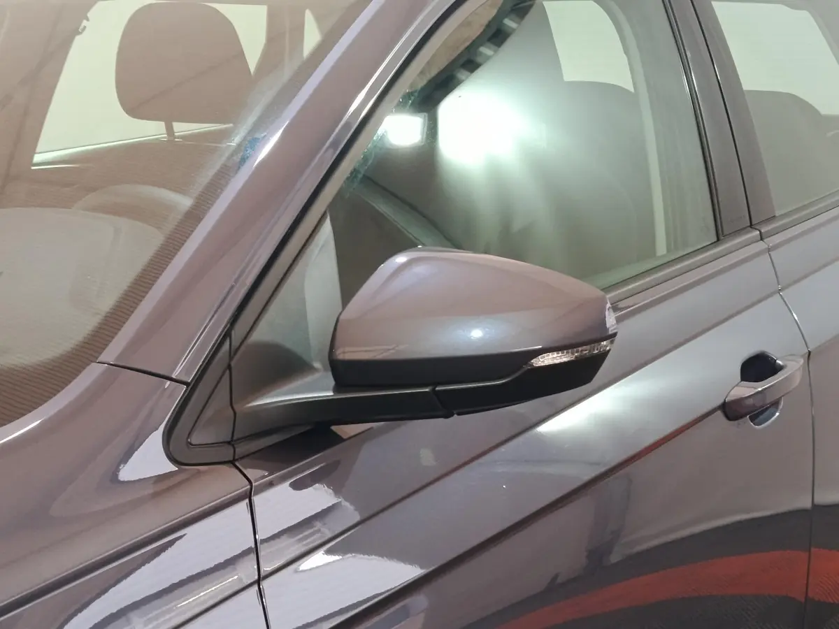Gros plan sur le rétroviseur côté gauche d'une Volkswagen Polo gris foncé avec poignée de porte visible.