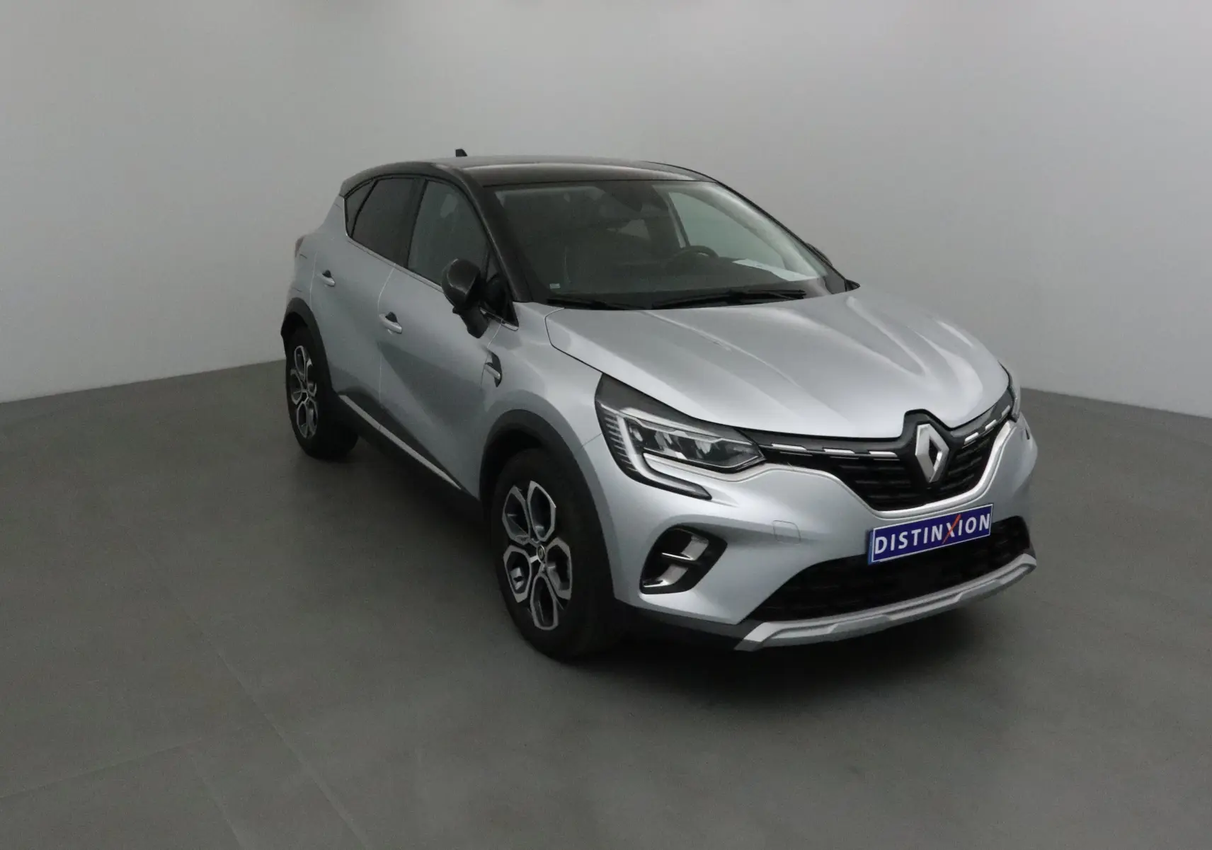 Renault Captur 2024 gris Highland avec toit noir, vue 3/4 avant droit mettant en valeur ses optiques LED et jantes 18 pouces.