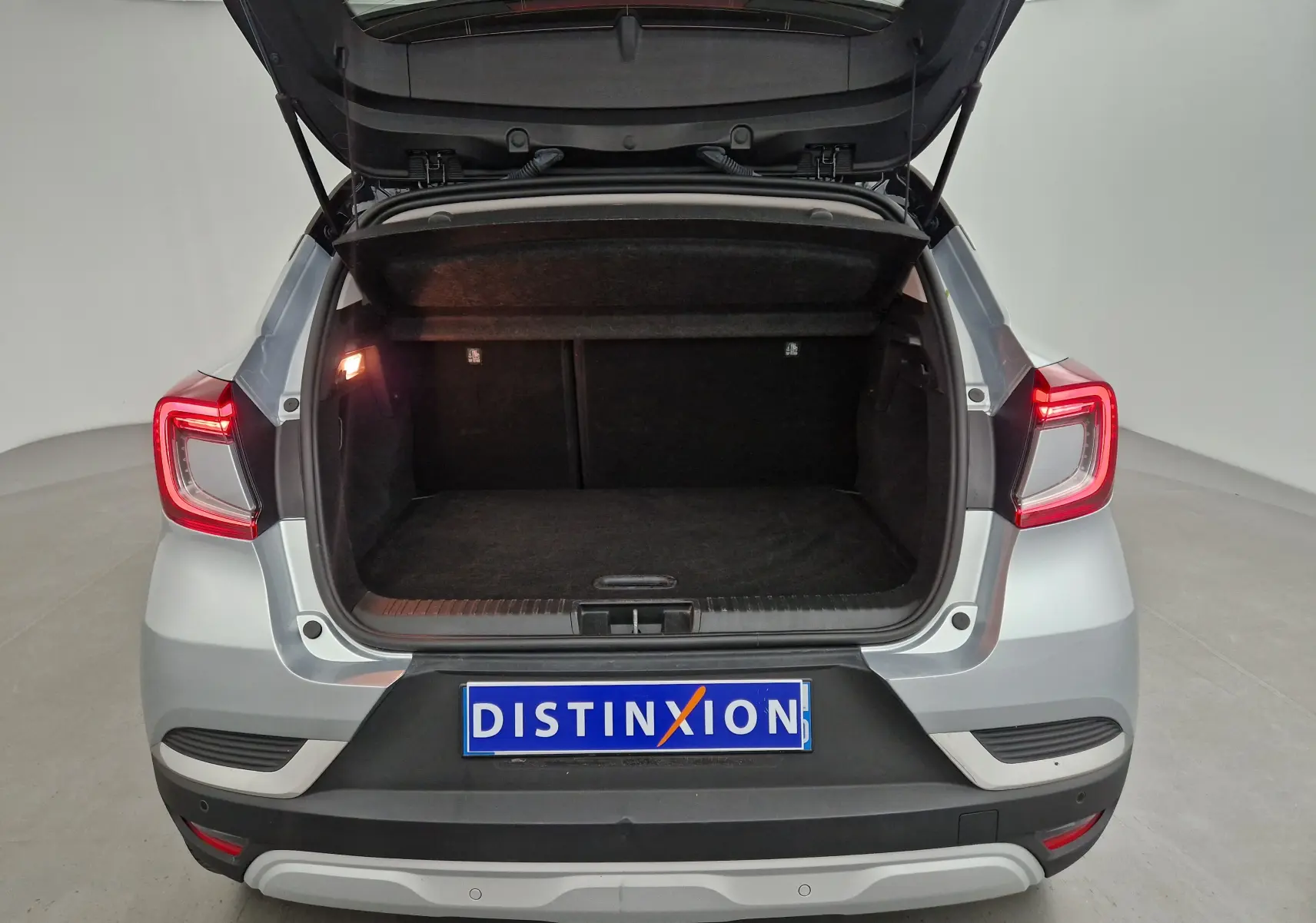 Vue arrière du Renault Captur gris Highland avec coffre ouvert et feux arrière allumés dans un studio.
