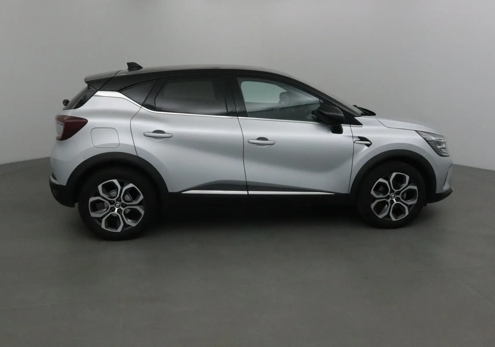 Profil droit du Renault Captur 2024 gris Highland avec toit noir et jantes alliage 18 pouces dans un studio.