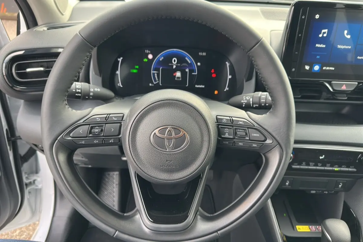 Vue rapprochée du volant et du tableau de bord numérique d'une Toyota Yaris blanche lunaire 2025 hybride.