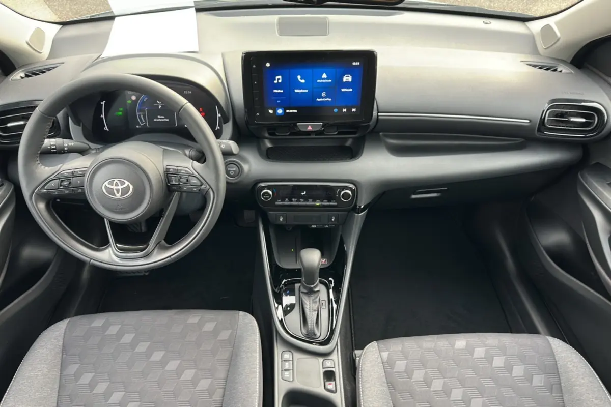 Intérieur de la Toyota Yaris 2025 hybride, vue frontale du tableau de bord avec écran tactile et levier de boîte automatique.