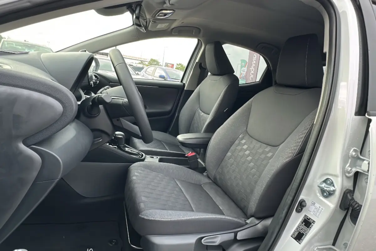 Vue intérieure côté conducteur de la Toyota Yaris 2025 blanc lunaire, sièges tissu gris avec motifs géométriques.