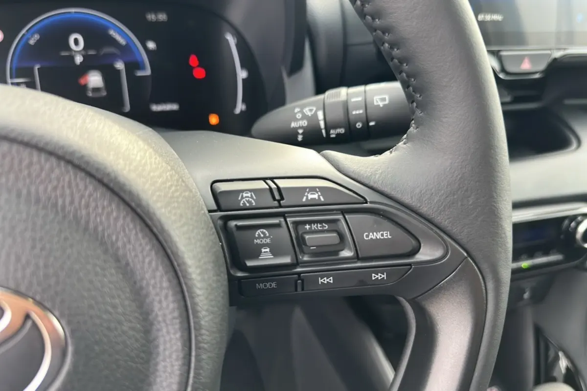 Gros plan sur le volant de la Toyota Yaris 2025 blanc lunaire, montrant les commandes de régulateur et d’aide à la conduite.