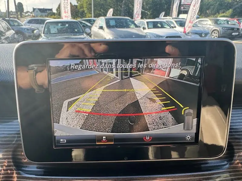 Écran tactile intérieur affichant la caméra de recul d’un Mercedes Classe V blanc cristal de roche métallisé en stationnement.