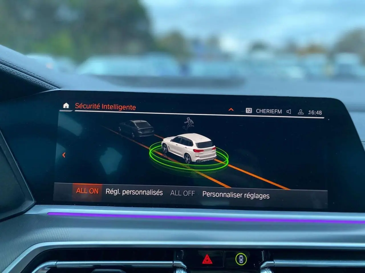 Écran intérieur du BMW X5 blanc 2022 montrant l'interface de sécurité intelligente avec visualisation 3D du véhicule en conduite.