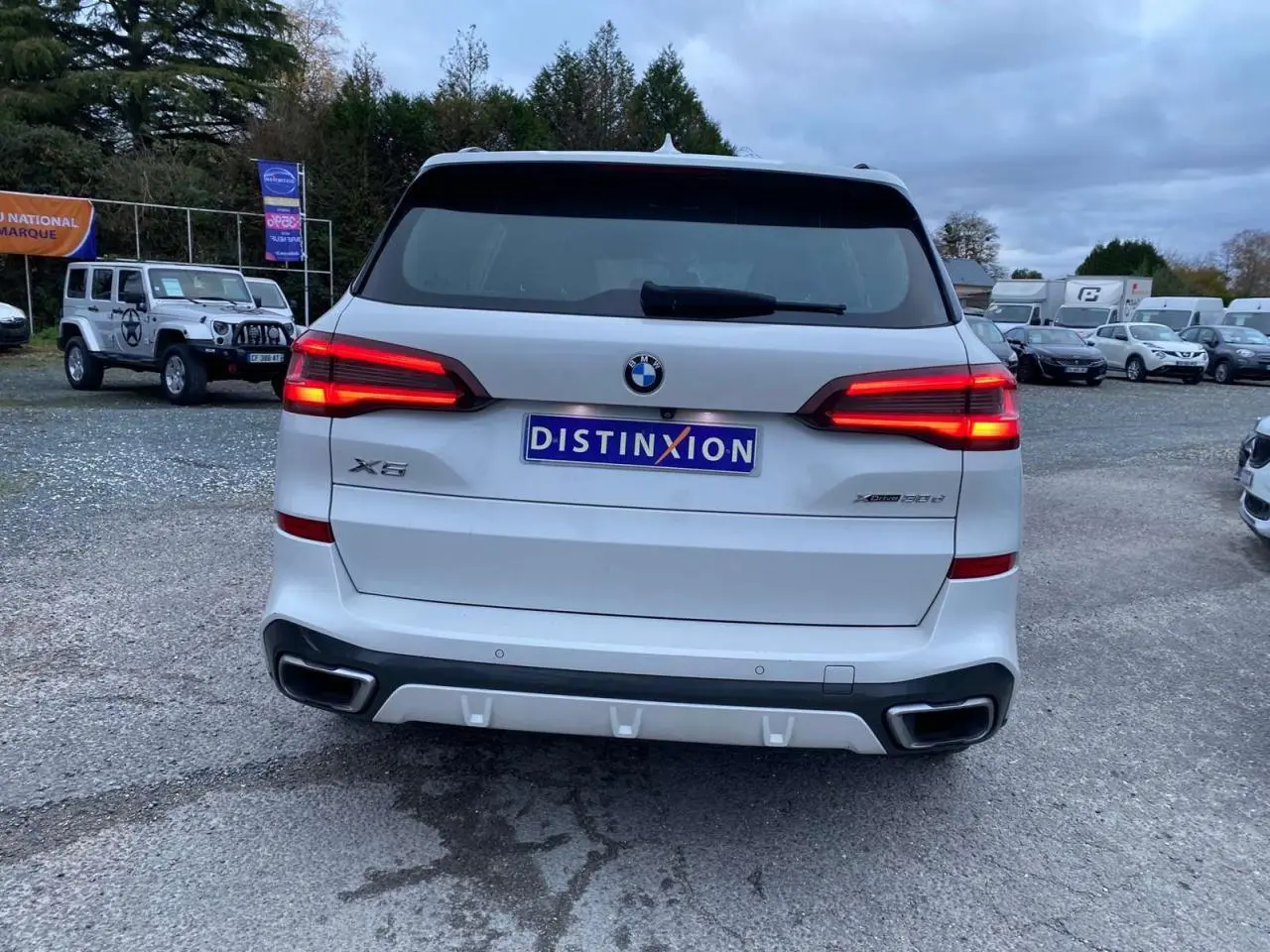 Vue arrière d'un BMW X5 blanc xDrive 30d 2022 avec feux allumés et double sortie d'échappement intégrée au pare-chocs.