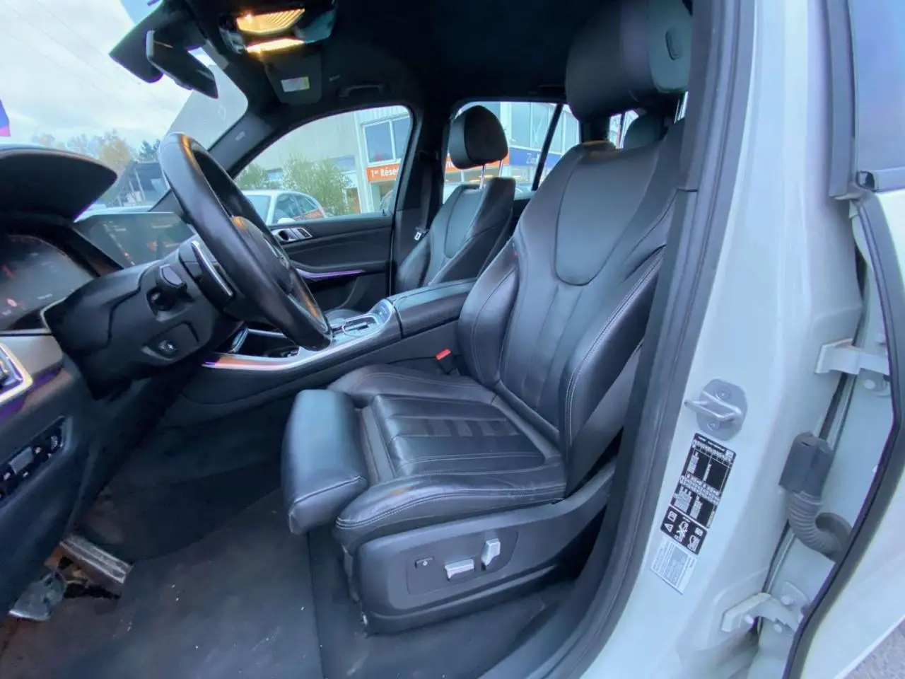 Vue intérieure côté conducteur du BMW X5 blanc 2022, sièges sport en cuir noir et tableau de bord moderne.