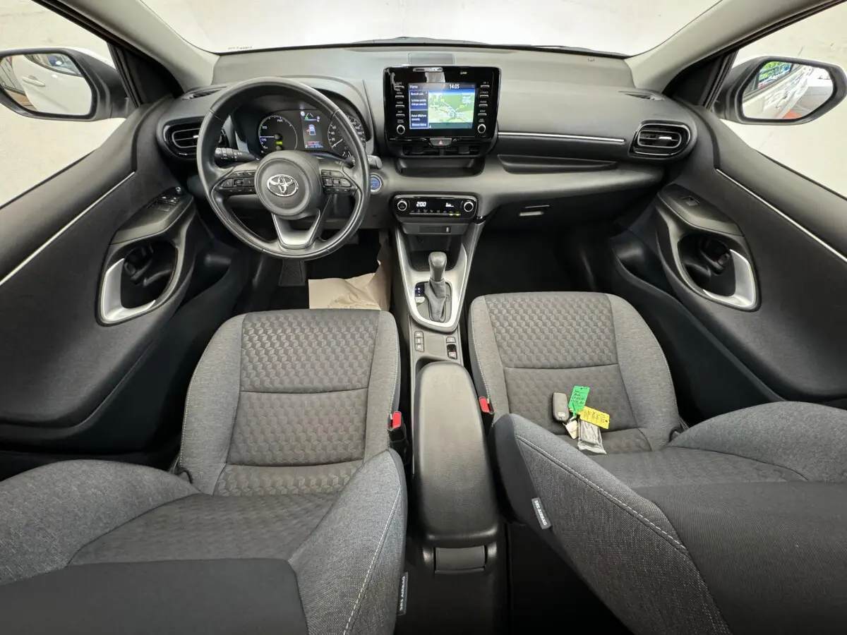 Vue intérieure avant de la Toyota Yaris hybride 2022, montrant tableau de bord noir et sièges tissu gris.
