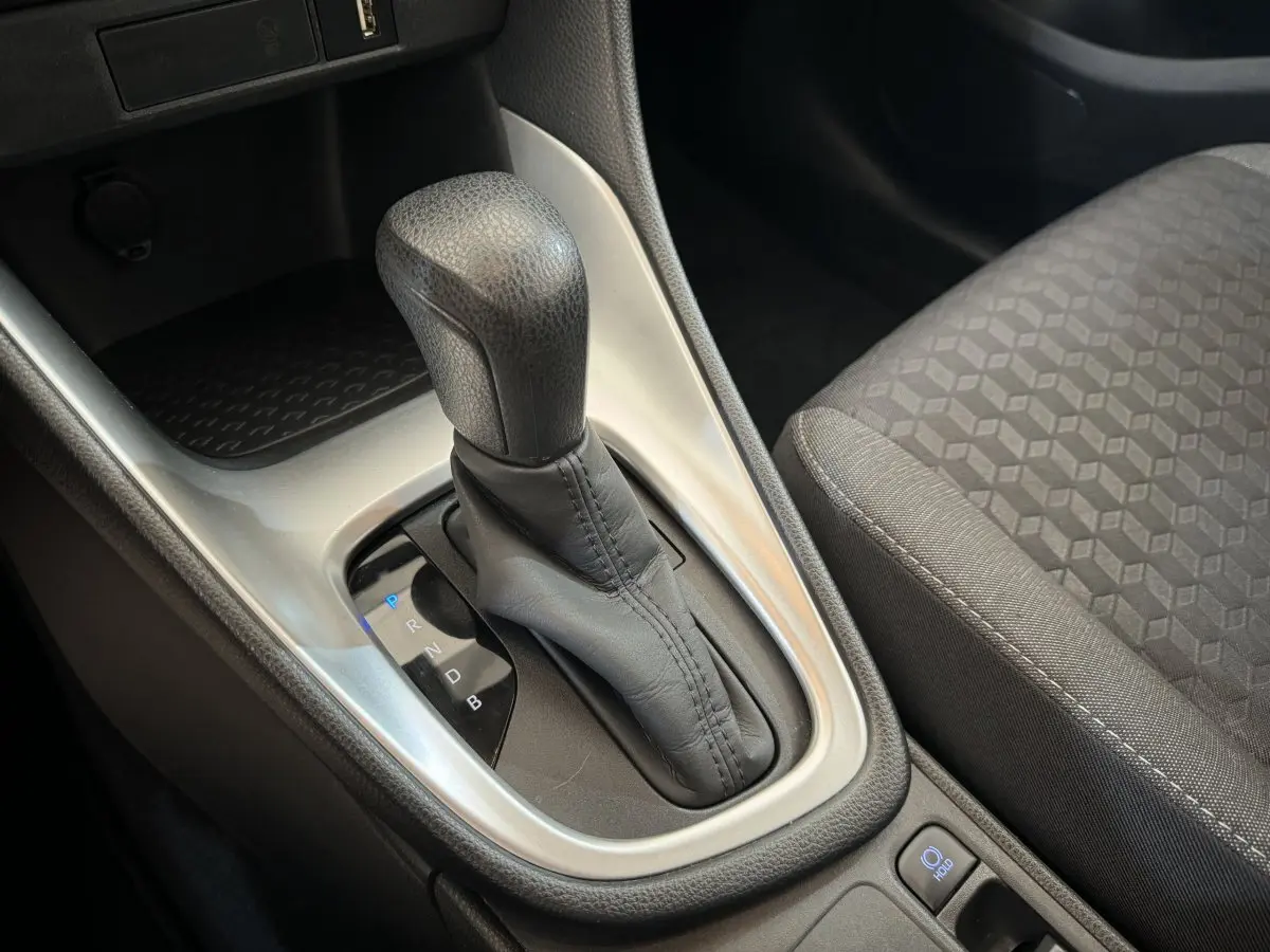 Gros plan sur le levier de vitesses automatique en cuir noir de la Toyota Yaris hybride, avec siège tissu gris à côté.