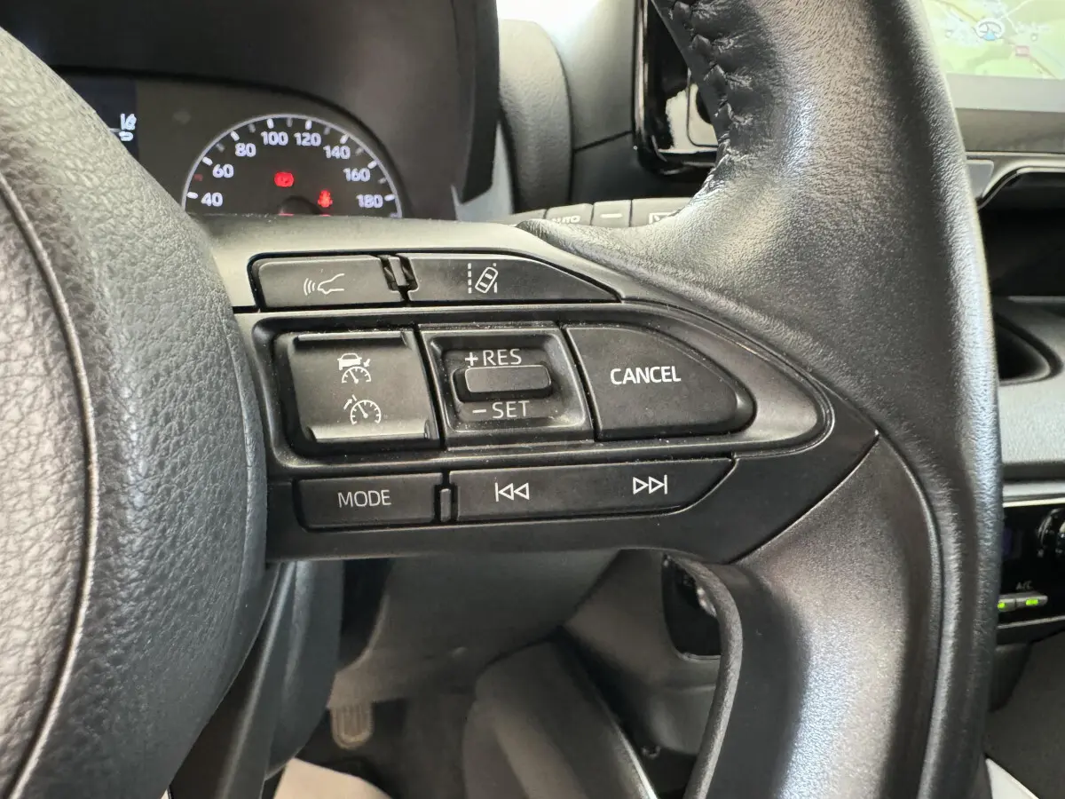 Gros plan sur les commandes au volant en cuir noir de la Toyota Yaris hybride 2022, avec tableau de bord et écran tactile en arrière-plan.