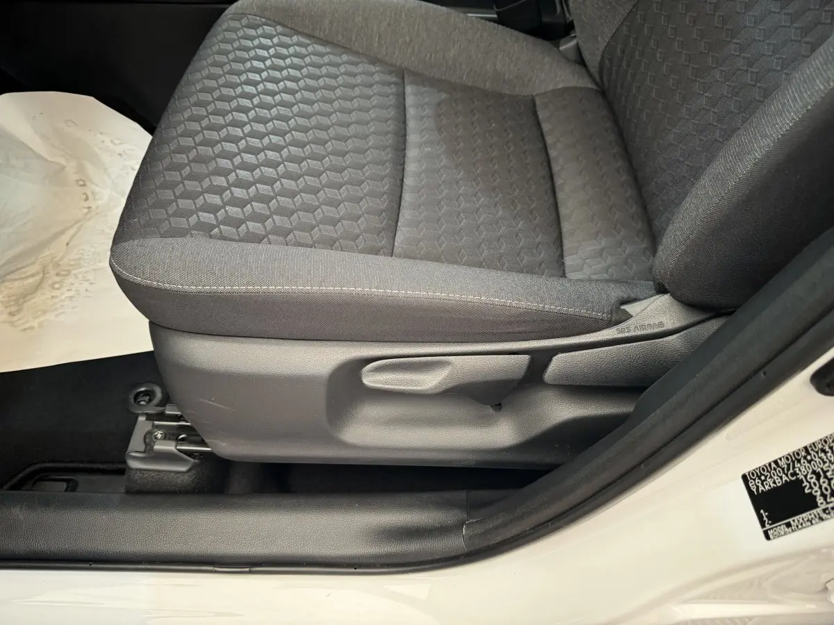Gros plan sur le siège avant droit gris foncé de la Toyota Yaris hybride blanche, montrant les réglages manuels et l'airbag latéral.