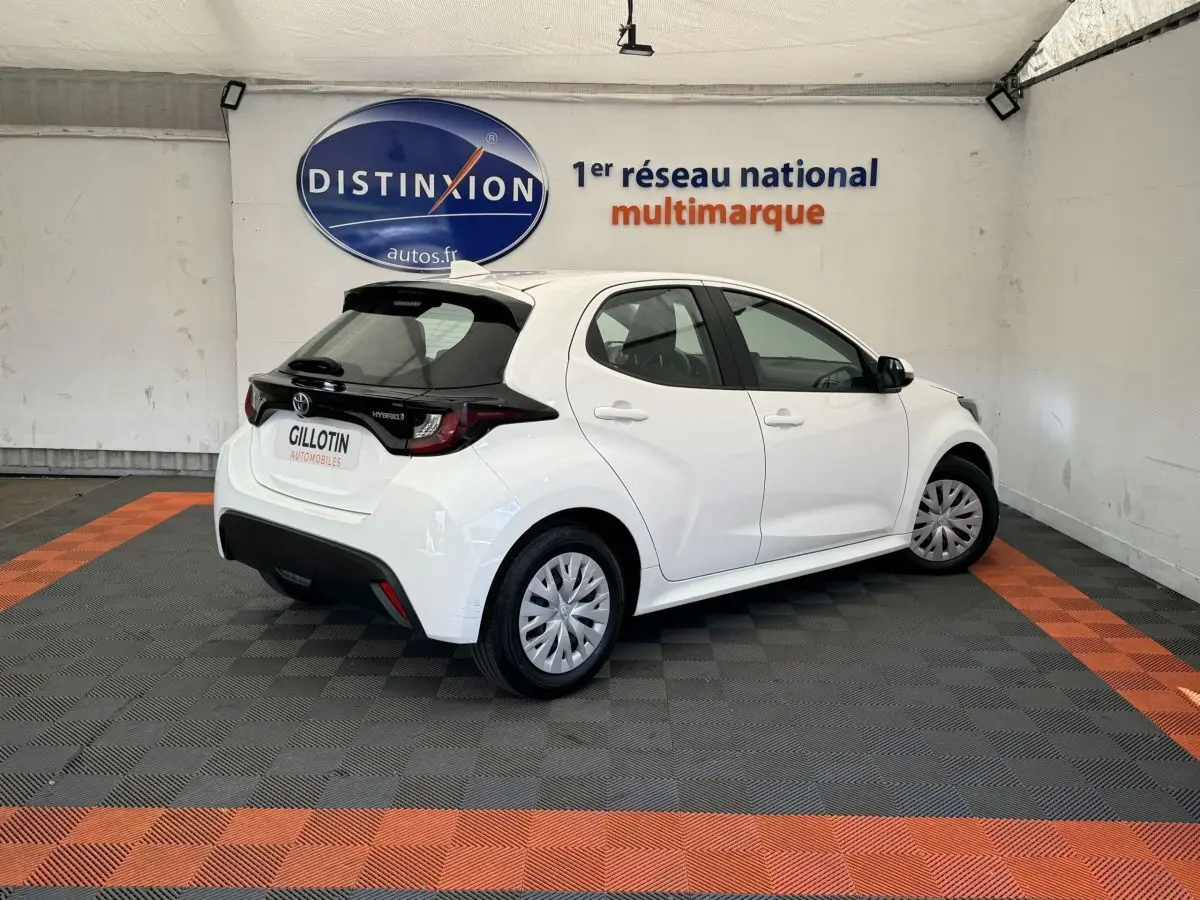 Toyota Yaris hybride blanche vue en 3/4 arrière droit, avec toit noir et jantes à enjoliveurs.