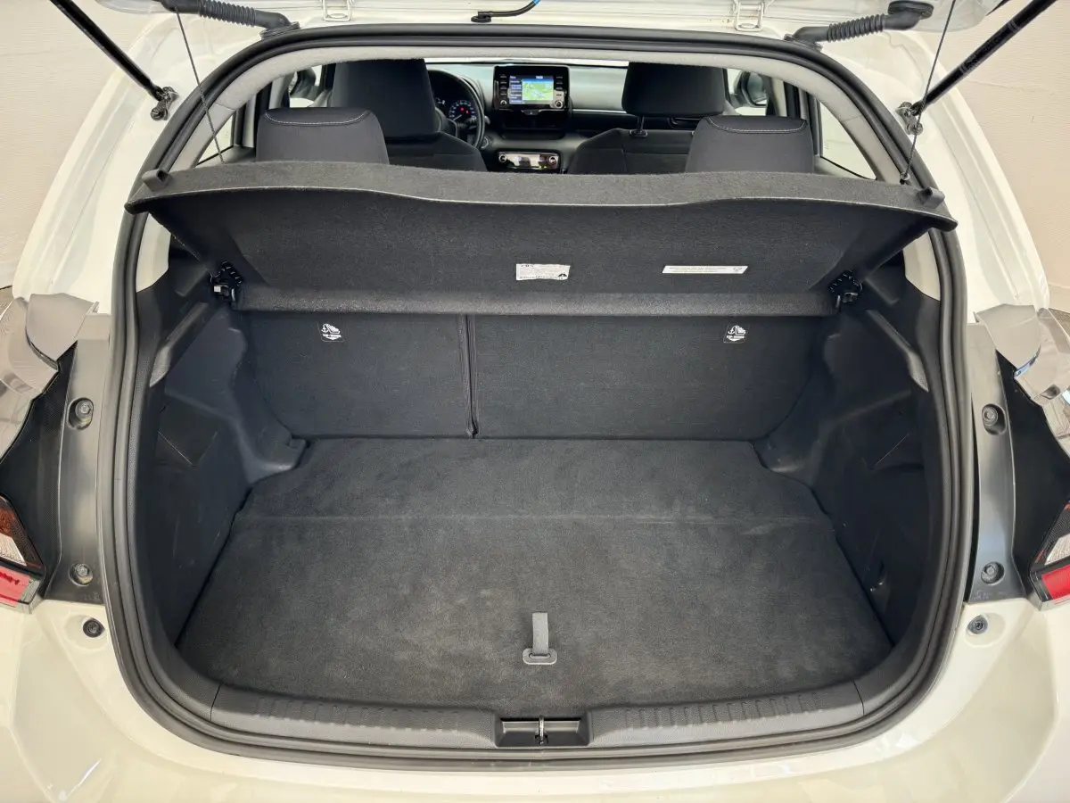 Vue arrière ouverte sur le coffre spacieux d'une Toyota Yaris hybride blanche 2022, avec intérieur noir et tablette de coffre relevée.