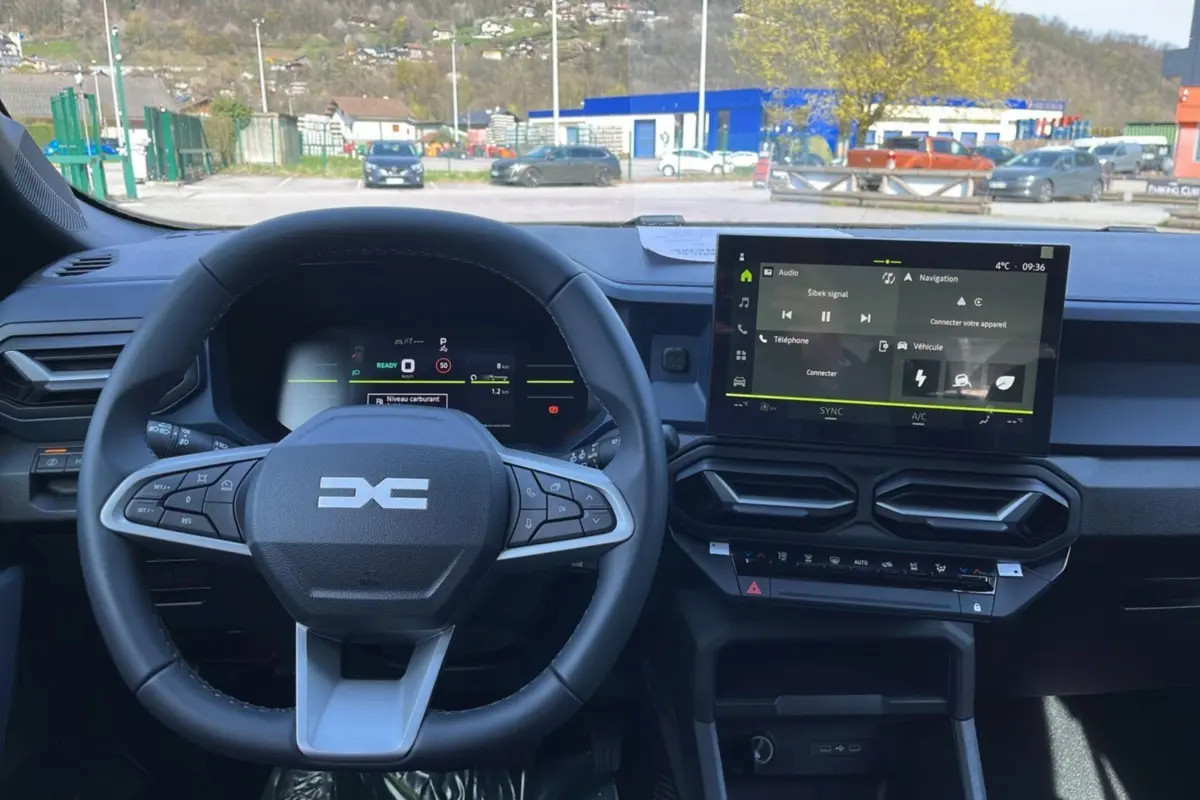 Vue intérieure centrée sur le volant cuir et l'écran tactile 10,1 pouces du tableau de bord du Dacia Bigster hybride.