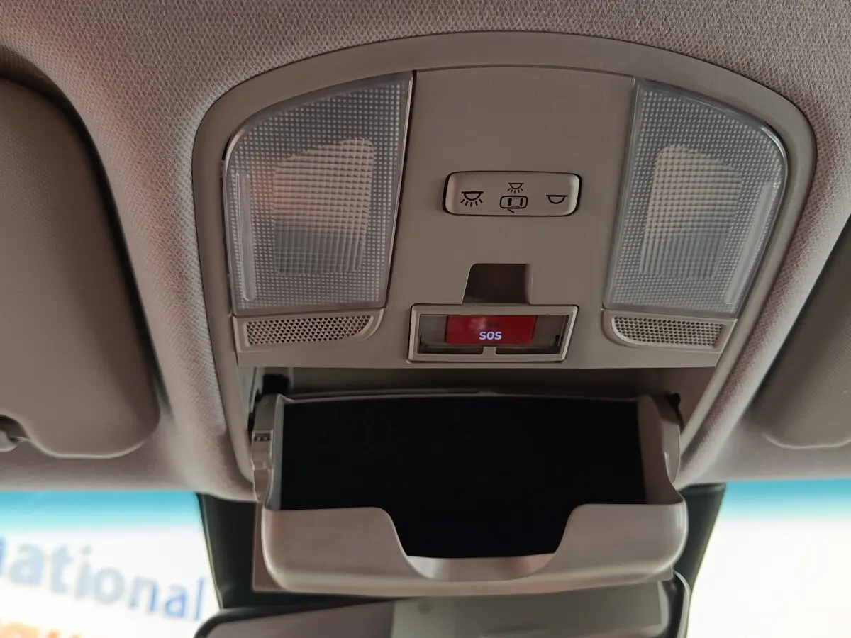 Vue intérieure du plafonnier gris clair avec éclairages, bouton SOS rouge et compartiment lunettes ouvert dans une Hyundai Kona électrique noire.