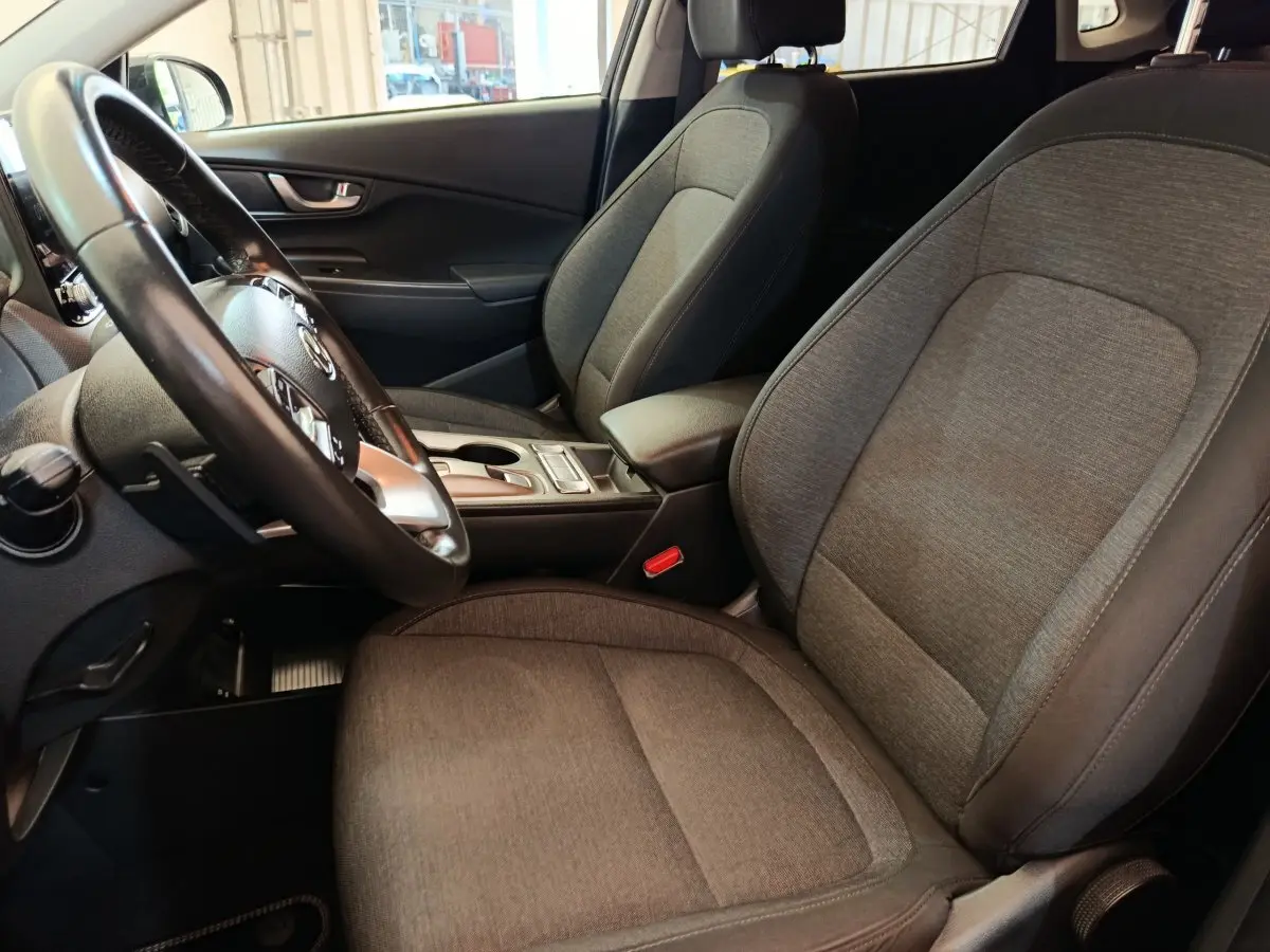 Intérieur avant droit du Hyundai Kona électrique 2023, sièges tissu gris et volant cuir multifonctions.