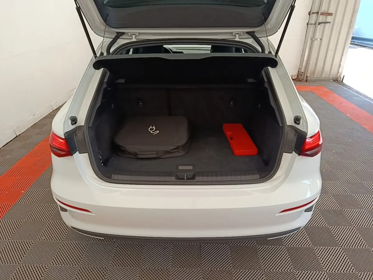 Vue arrière d'un Audi A3 blanc 2022 avec coffre ouvert montrant un sac de charge et une trousse rouge à l'intérieur.