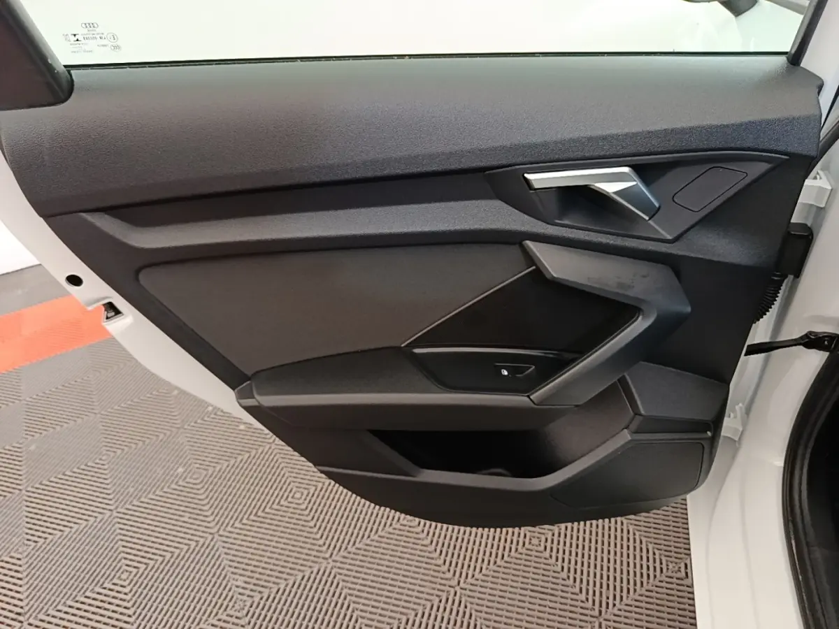 Vue intérieure côté gauche de la porte avant blanche d’une Audi A3 40 TFSI e avec garniture noire et poignée argentée.