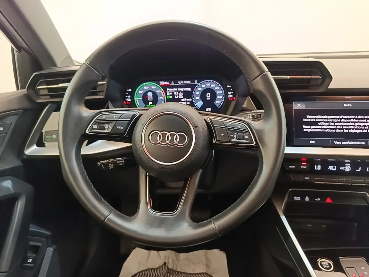 Vue centrée sur le volant cuir noir et le tableau de bord digital d'une Audi A3 40 TFSI e blanche de 2022.