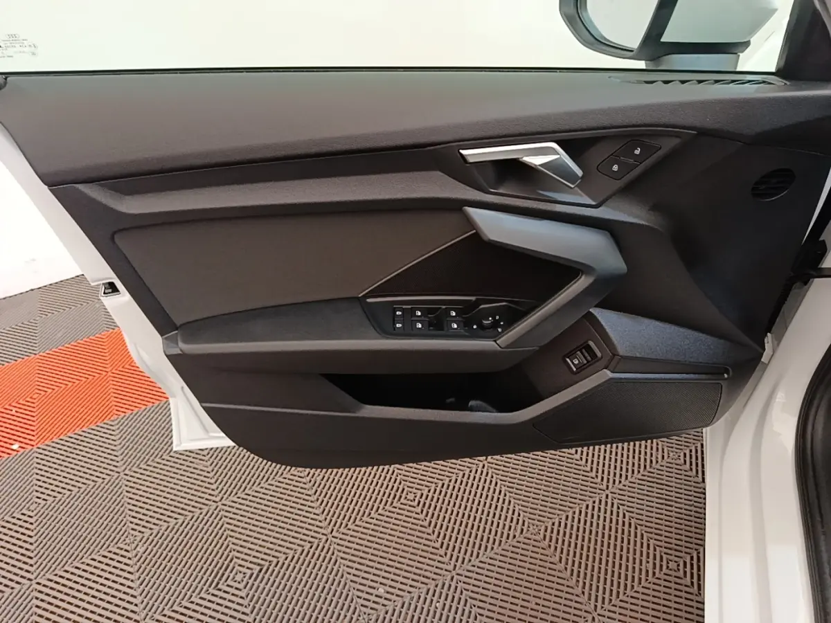 Vue intérieure de la porte avant gauche blanche d'Audi A3 40 TFSI e 2022 avec commandes électriques et poignée angulaire.