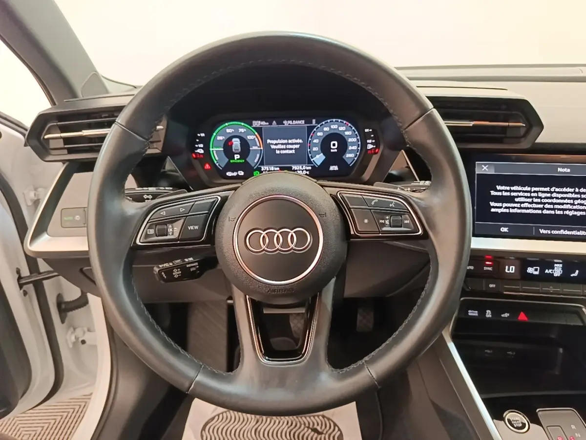 Vue centrée sur le volant cuir noir et le tableau de bord digital d'une Audi A3 blanche hybride rechargeable 2022.