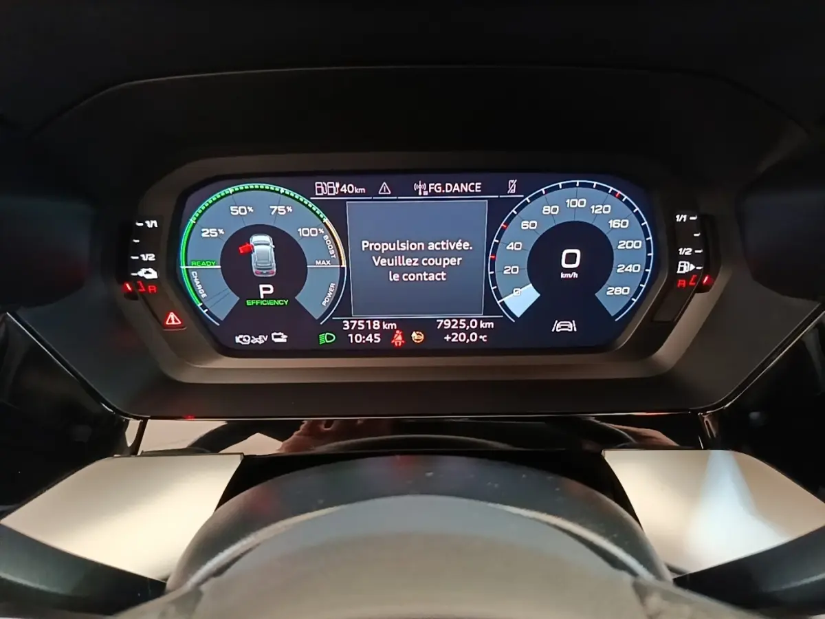 Vue rapprochée du tableau de bord numérique de l'Audi A3 hybride blanche, affichant les compteurs et alertes de conduite.