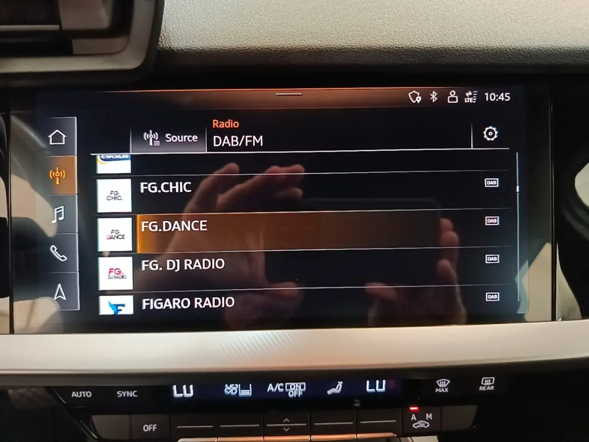 Écran tactile central de l'Audi A3 blanc, affichant les stations radio DAB/FM en intérieur.
