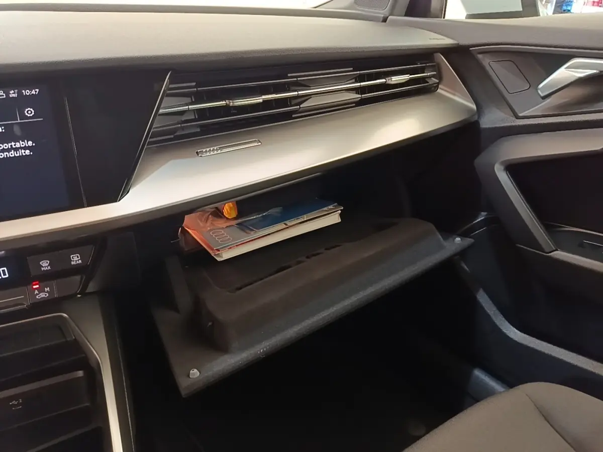 Intérieur Audi A3 40 TFSI e 2022, vue côté passager sur boîte à gants ouverte avec documents et tableau de bord noir et beige.
