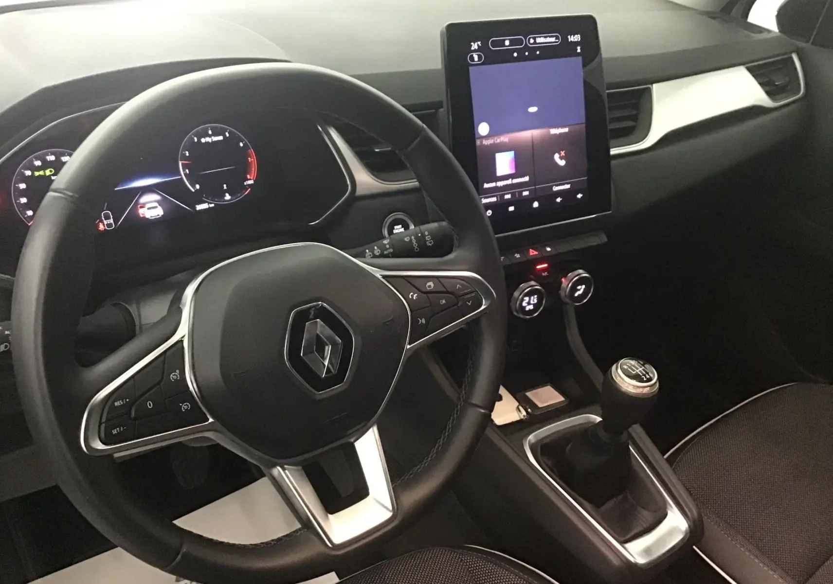 Vue intérieure du tableau de bord et volant Renault Captur blanc nacré/ noir, avec écran tactile vertical et levier de vitesse manuel.