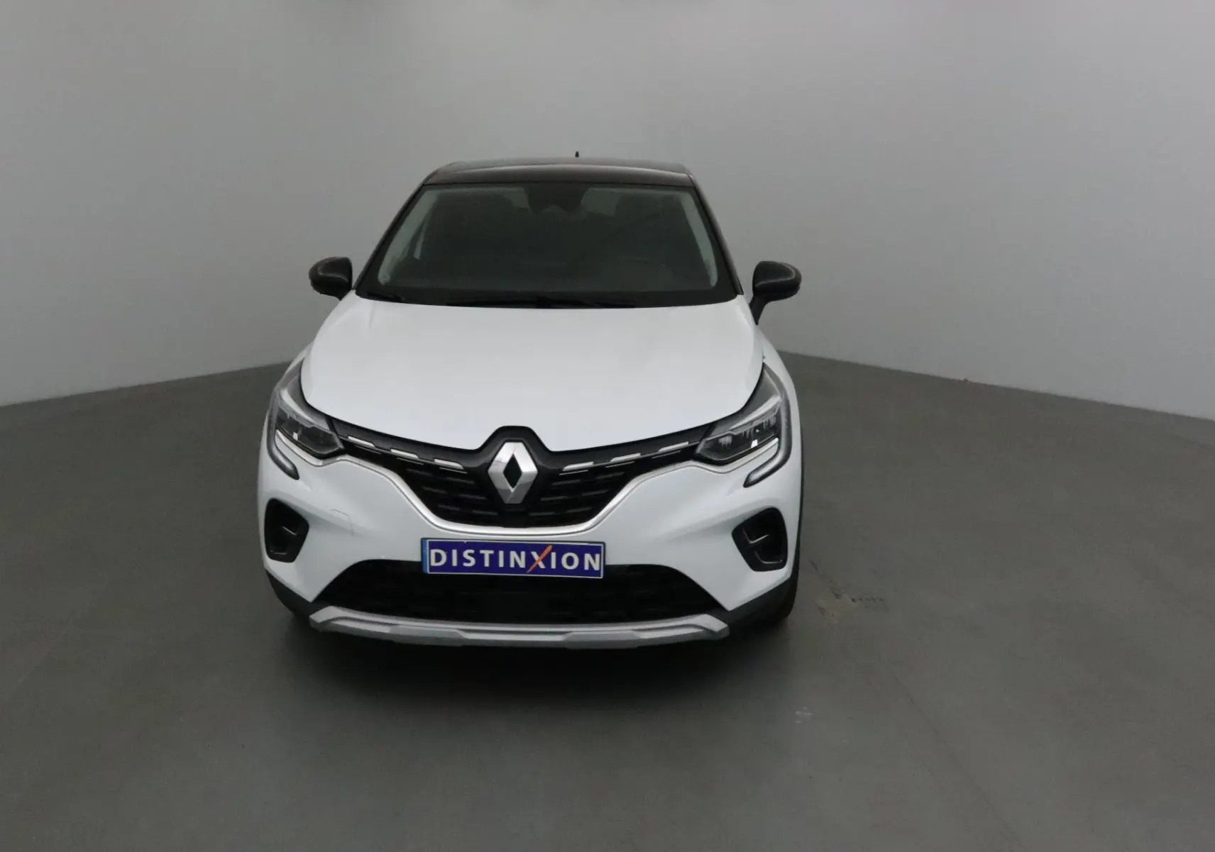 Vue frontale d'un Renault Captur blanc nacré avec toit noir, calandre noire et logo Renault bien visible.