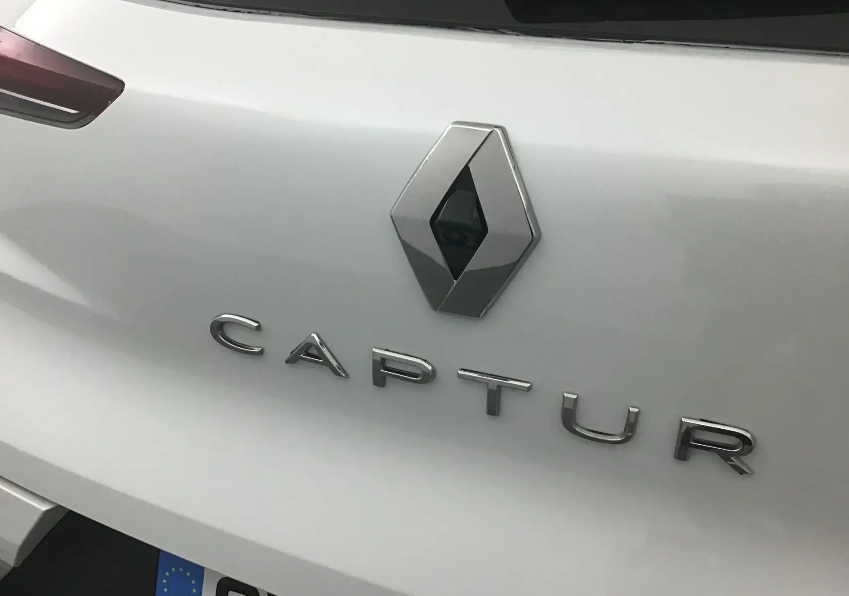Gros plan sur l'arrière blanc nacré du Renault Captur 2024 avec logo et caméra de recul intégrée.