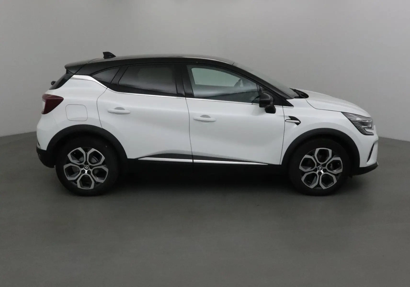 Profil côté gauche du Renault Captur 2024 blanc nacré avec toit noir et détails noirs contrastants.