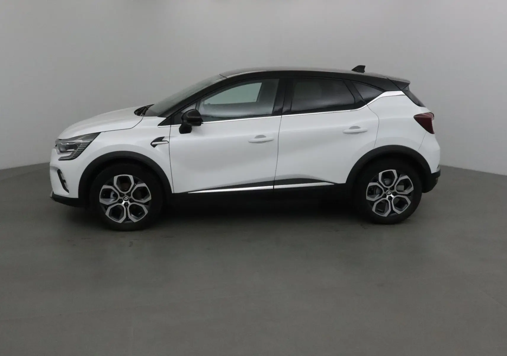 Profil côté gauche d'un Renault Captur blanc nacré avec toit noir, jantes alliage et lignes modernes.