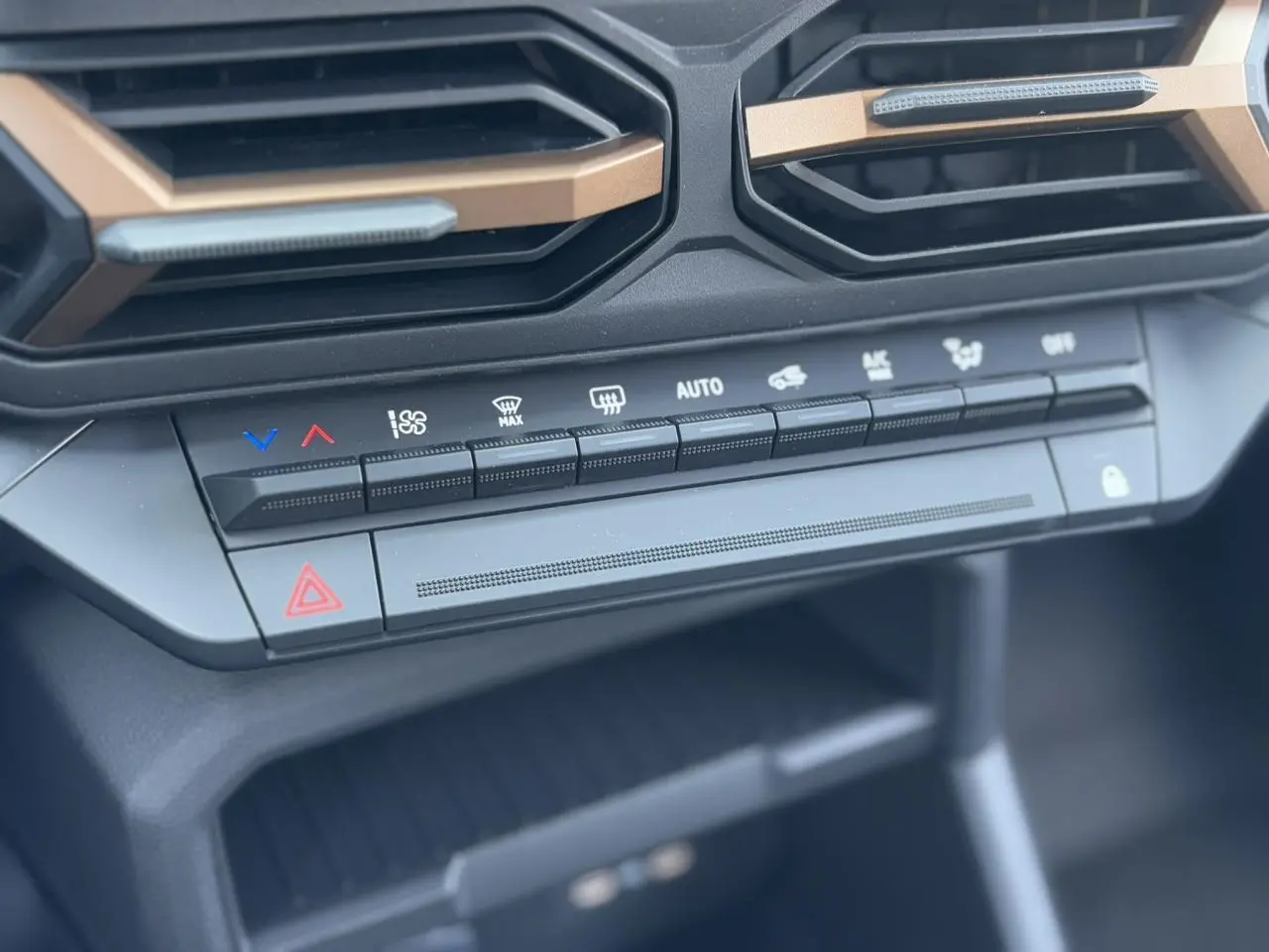 Gros plan sur la console centrale du Dacia Duster 2025, montrant les commandes de climatisation et les aérateurs avec inserts cuivrés.