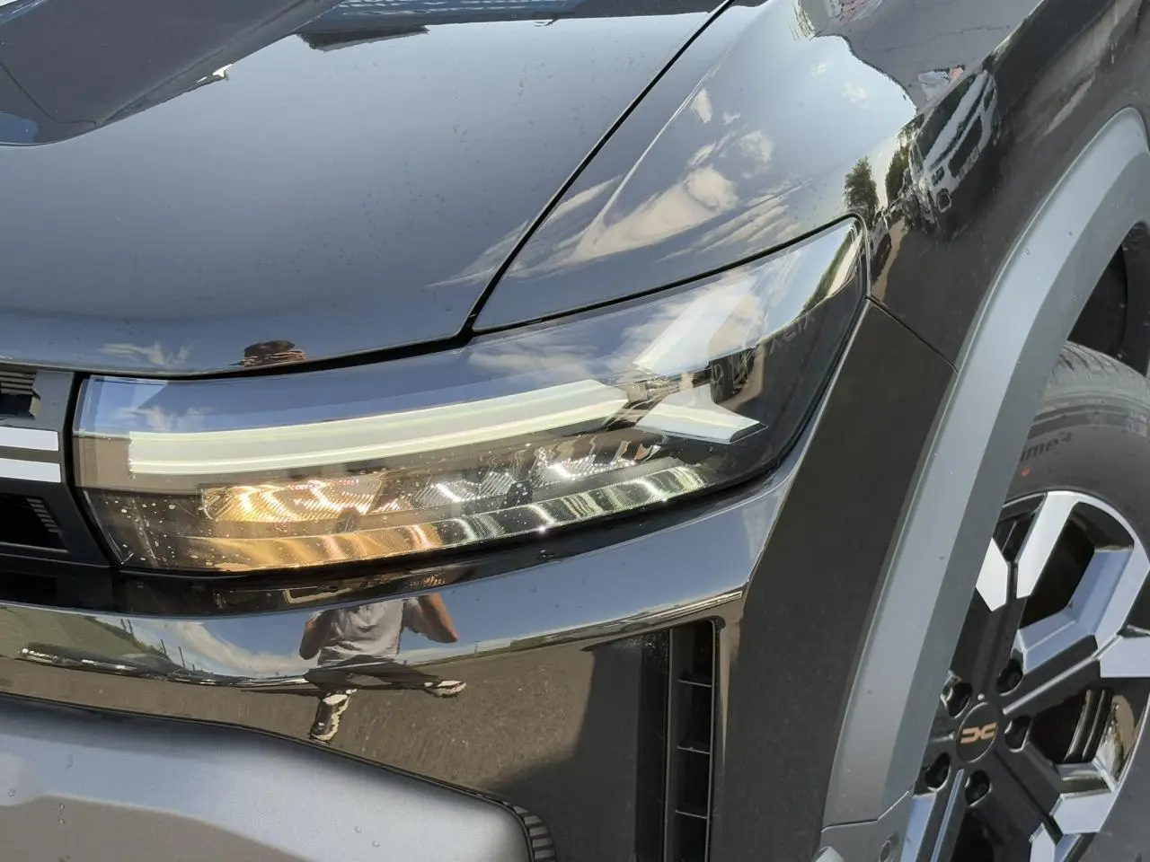 Gros plan sur le phare avant droit et la jante alliage 17" du Dacia Duster noir nacré 2025.
