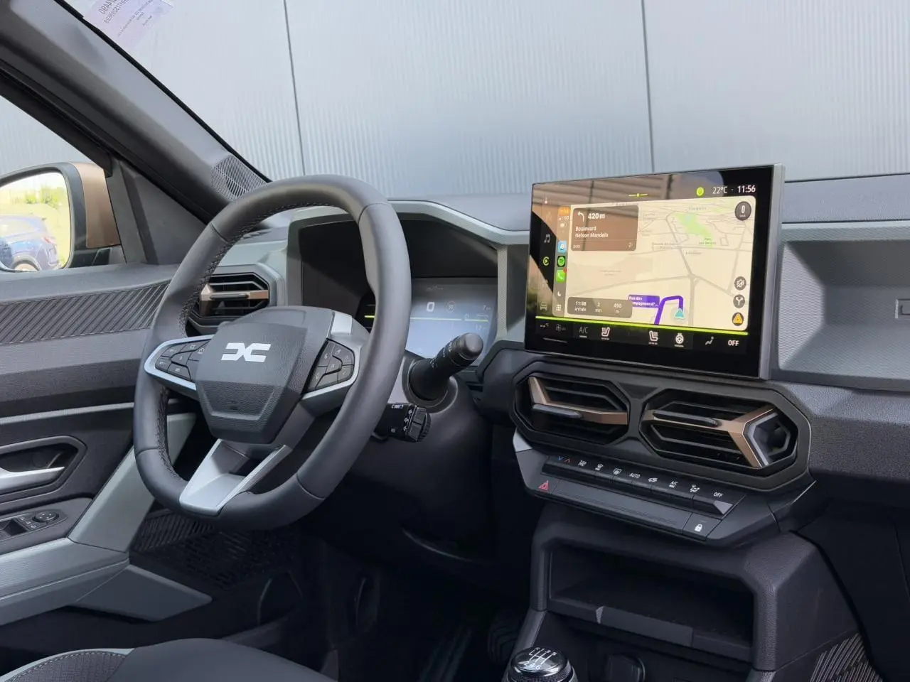 Vue intérieure côté conducteur du tableau de bord du Dacia Duster 2025 avec écran tactile GPS et volant multifonctions.