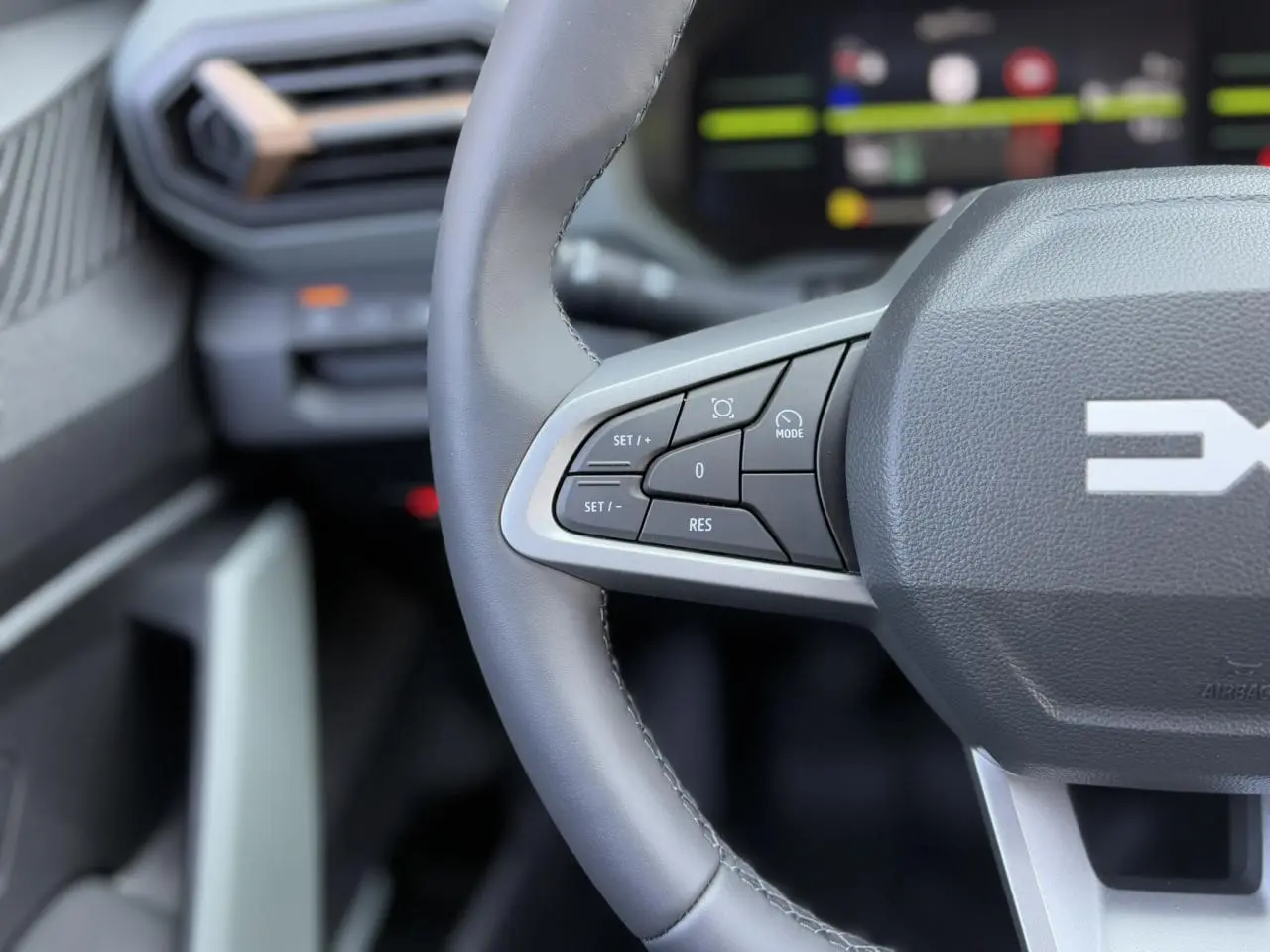 Gros plan sur le volant gris du Dacia Duster 2025 avec commandes intégrées et tableau de bord digital flou en arrière-plan.
