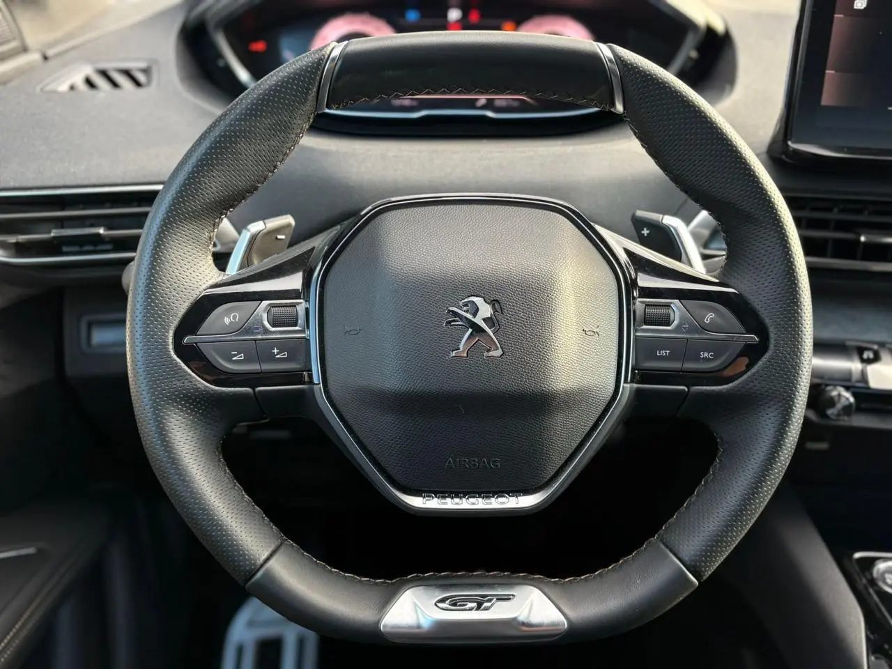 Volant cuir perforé Peugeot 3008 GT vu de face avec badge GT et commandes multifonctions intégrées.