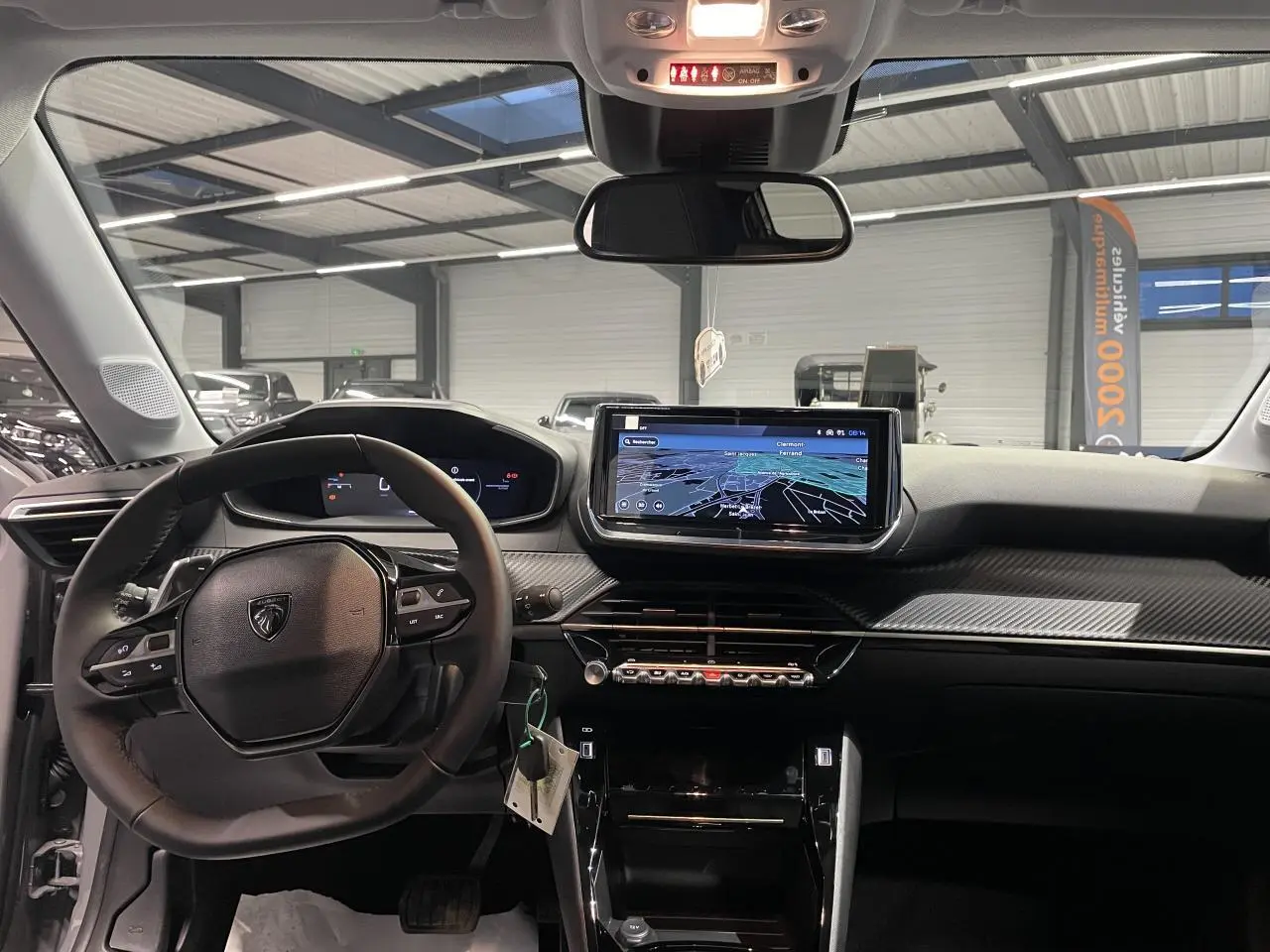 Vue intérieure avant du tableau de bord noir de la Peugeot 208 1.2i Hybrid avec écran tactile et volant compact cuir.